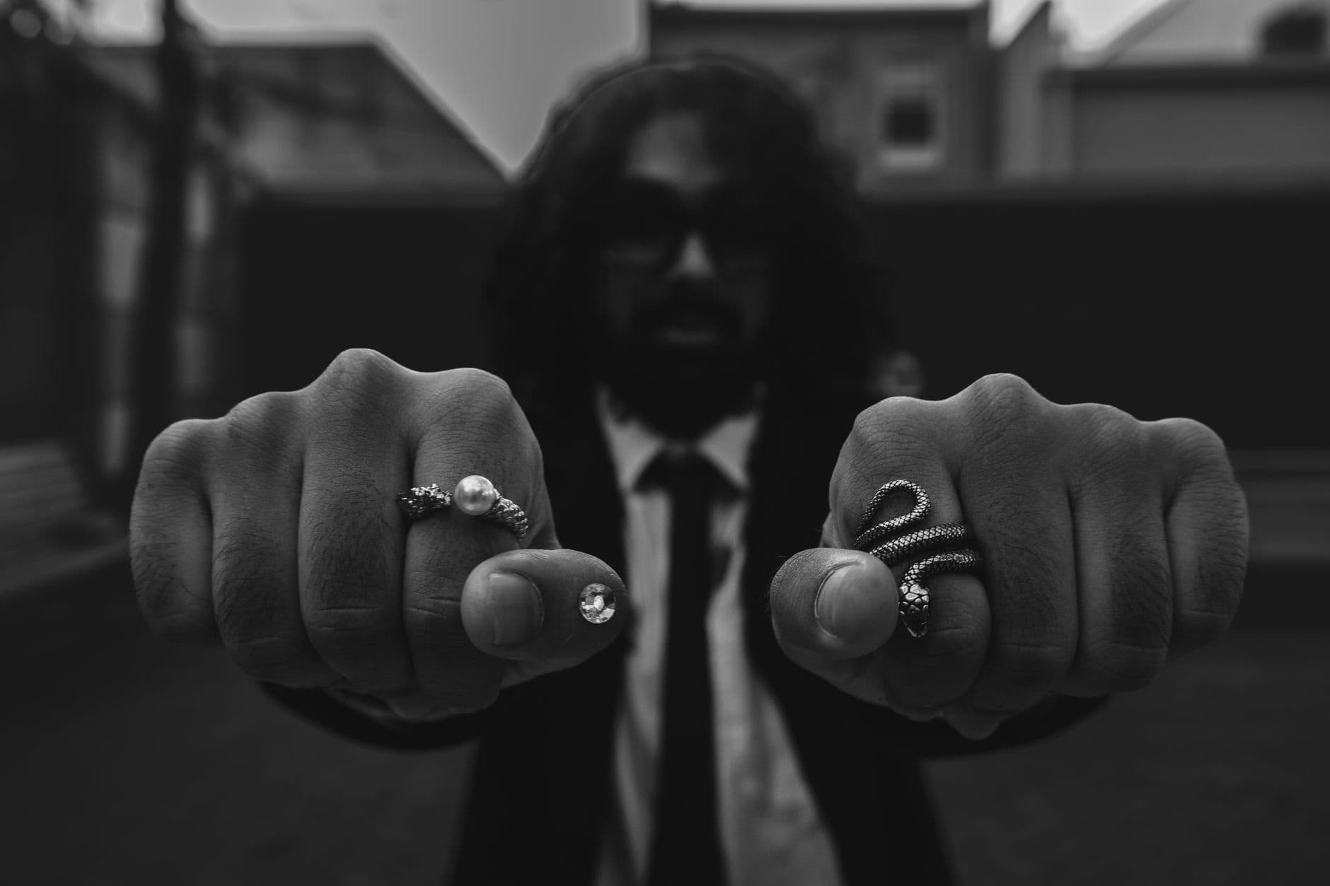Black and white photo of a man displaying rings in an urban setting, emphasizing fashion.