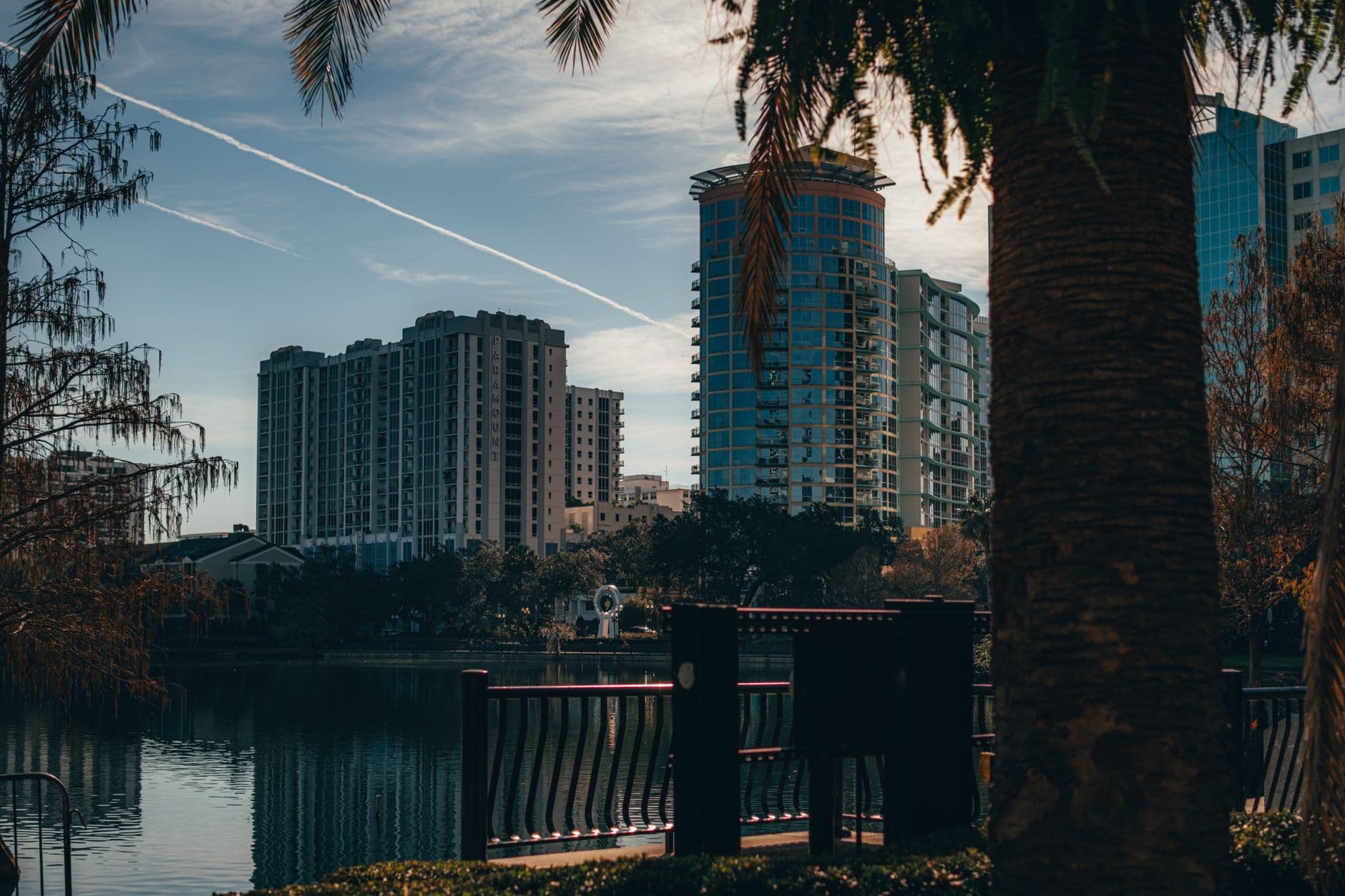 View of Orlando's modern skyline reflecting on a tranquil lake, surrounded by trees.
