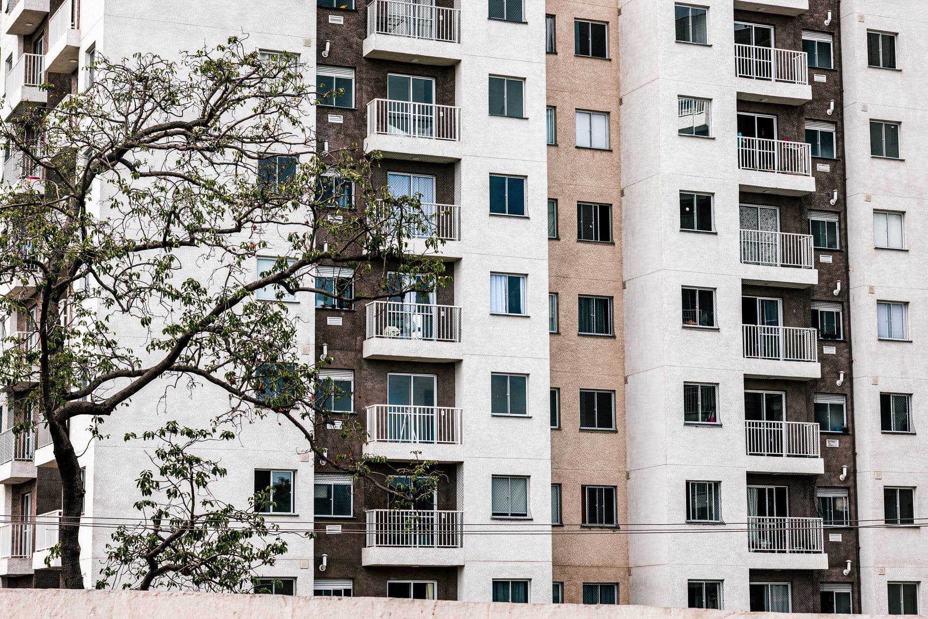 Exterior view of a modern apartment building with balconies and a tree, showcasing urban architecture.